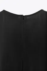 Vestido midi negro de tejido fluido, con cuello redondo y sisa. Cierre trasero con cremallera oculta.