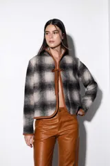Chaqueta corta de paño a cuadros en tonos beige y negro, con cuello mao y ribete de cuero marrón en todo el contorno. Se ata con lazos de cuero en el centro y tiene bolsillos laterales.