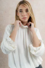 Blusa color crema de tela tejida 100% lana, con cuello fruncido y mangas largas con puños elásticos.