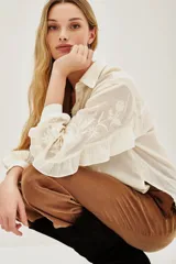 Camisa de algodón color blanco roto, con cuello camisero, mangas largas con volados y bordados florales en las mangas.