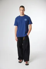 Remera de manga corta color gris oscuro, con cuello redondo y un pequeño parche cuadrado con una 'X' estampada en el pecho izquierdo.