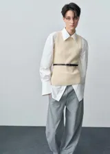 Chaleco de punto color crema, con cuello redondo y diseño sin mangas. Ajustado al cuerpo y con cinturón fino de cuero marrón.