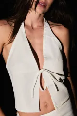 Top blanco de gabardina con tiras ajustables en cuello y delantero, y recortes irregulares.