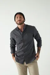 Camisa de hombre color gris oscuro con efecto stone wash, fit regular, mangas largas, cuello clásico, cierre frontal con botones, dos bolsillos frontales con solapa abotonada y puños abotonados.