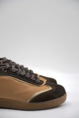 Zapatillas urbanas de cuero color beige con puntera y cordones marrones. Presentan un panel de animal print en el talón y suela de goma color caramelo.