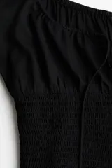 Blusa negra con escote cuadrado, mangas cortas abullonadas con elástico en hombros y puños, cintura fruncida y abertura con cordón para ajustar en el delantero.