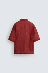 Camisa color ladrillo con estampado de flores en relieve, corte relaxed fit, cuello bowling, manga corta, bajo con aberturas laterales y cierre frontal con botones.