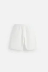 Bermuda relaxed fit color blanco confeccionada en tejido interlock de algodón con elasticidad. Cintura elástica ajustable con cordón interior. Bolsillos laterales y detalle de bolsillo trasero de plastrón.