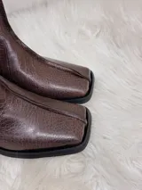 Botas cortas color chocolate con textura de cocodrilo, punta cuadrada y tacón bajo. Cuentan con cierre lateral.