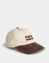Gorra de béisbol color beige con visera marrón y bordado frontal con la frase "Express Yourself" en marrón. Cuenta con botón superior marrón y regulador trasero metálico.