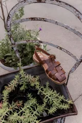 Sandalias de cuero marrón con tiras entrecruzadas y hebilla dorada al tobillo.