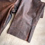 Pantalón de cuero negro, de corte recto y tiro alto, con bolsillos delanteros y traseros.