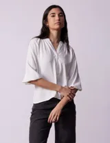 Blusa blanca de gasa marca Sioni, con cuello a la base y escote en V. Tiene abertura central con botones y mangas 3/4 con terminación fruncida.