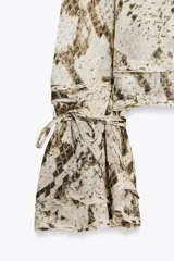 Blusa de viscosa con estampado de piel de serpiente en tonos beige y marrón. Tiene cuello redondo con lazo ajustable, mangas largas acampanadas con cordones en los puños y bajo recto.