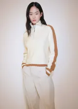 Sweater de punto grueso color crema con cuello alto con cierre de cremallera y detalle de rayas marrones en contraste en mangas y ruedo.