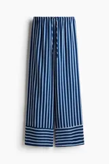 Pantalón de corte holgado en sarga con estampado a rayas verticales azules y blancas. Modelo de talle alto con cintura elástica y cordón de ajuste fino.