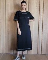 Vestido midi negro con cuello redondo y mangas cortas. Presenta dos bolsillos cuadrados en el pecho y ribetes blancos en cuello, mangas, bolsillos y ruedo.