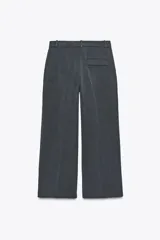Pantalón negro de tiro alto con trabillas, bolsillos laterales y pinzas. Cierre frontal con cremallera, botón interior y gancho metálico.