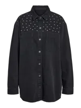 Camisa oversize de denim negro con cuello clásico, cierre con botones, bolsillos frontales y tachas plateadas en la parte superior.