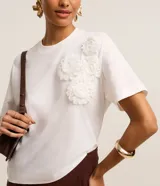 Blusa blanca de algodón con cuello redondo, mangas cortas y apliques de flores de tela en el hombro.