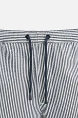 Short de baño con textura seersucker a rayas verticales azul marino y blanco. Tiene cintura elástica ajustable con cordón, bolsillos frontales y traseros, aberturas laterales en el bajo y forro interior.