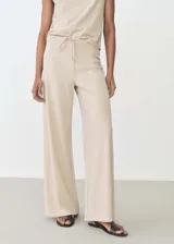 Pantalón largo de mujer color beige, de corte ancho y tiro alto, con cintura elástica y lazo ajustable.
