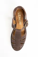 Sandalia cangrejera de gamuza color marrón oscuro, con puntera cerrada y tiras entrecruzadas. Posee tira de ajuste con hebilla metálica dorada en el tobillo y suela de goma plana.