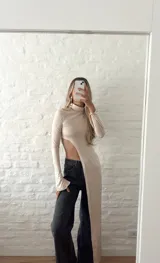 Top de lycra color beige, con cuello alto y mangas largas. Presenta un corte asimétrico en la parte inferior.