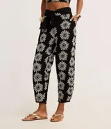 Pantalón zanahoria de cintura alta, confeccionado en laise negro con bordado floral blanco y lazo en la cintura.