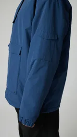 Campera pullover azul marino con capucha, cierre parcial en el cuello y bolsillo tipo canguro con solapa. Tiene un bolsillo con cierre en la manga izquierda y puños elásticos.