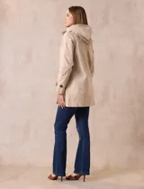 Gabardina impermeable color beige, marca Weatherproof, con abertura central con botones, bolsillos delanteros y capucha desmontable.