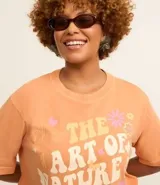 Remera color durazno de corte cuadrado con cuello redondo y mangas cortas. Estampa frontal con flores y la frase "The art of nature is blooming".