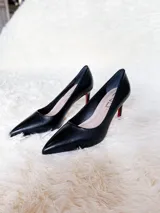 Zapato de tacón alto Iara, color negro, confeccionado en cuero. Tiene punta fina y un pequeño detalle en rojo en el tacón.