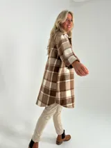 Sobrecamisa larga a cuadros marrones y blancos, con cuello camisero, cierre frontal con botones y bolsillos de parche en el pecho.