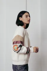 Sweater de punto color crema con cuello redondo y mangas largas con diseño geométrico en tonos beige, rojo, azul y blanco.