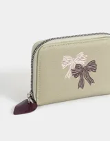 Billetera pequeña de cuerina color blanco con estampado de lazos rosas y corazones. Tiene cierre circundante y tirador de goma.