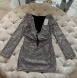 Vestido corto plateado de lentejuelas con mangas largas acampanadas y espalda descubierta que se ata con tiras.