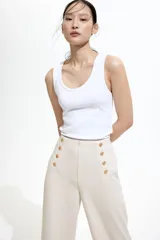 Pantalón de vestir color crema, de tiro alto y corte palazzo, con detalle de doble botonadura dorada en la parte superior.