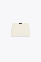 Falda pantalón color crema de tiro bajo con cintura asimétrica, bolsillos delanteros de vivo y cierre lateral con cremallera oculta.