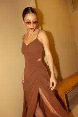 Vestido largo color marrón, con escote corazón, tirantes finos y falda con frunces laterales y tajo frontal.