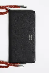 Minibolso negro de estructura blanda con asa de mano de cordón rojo y asa larga extraíble. Presenta logo metálico, acabados metálicos y cierre con botón de presión. Incluye tarjetero interior e interior con logo estampado.