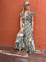 Vestido largo de seda color crema con estampado de hojas y flores en negro. Tiene escote en V cruzado, mangas cortas con volados y lazo ajustable en la cintura.