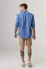 Camisa de manga larga azul denim, con cuello clásico y cierre frontal con botones. Mangas con puños abotonados y corte recto.