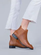 Bota tipo chelsea de cuero color marrón con textura grabada tipo reptil. Presenta paneles elásticos laterales a tono y suela de caucho termoplástico con tacón bajo.