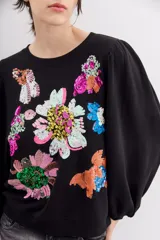 Buzo negro de algodón con cuello redondo y mangas largas abullonadas. Presenta apliques de flores bordadas con lentejuelas.