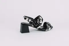 Sandalias de cuero con estampado animal print de vaca en blanco y negro, con detalles de tachas plateadas. Tienen correa trasera con hebilla y taco cuadrado de 5 cm.