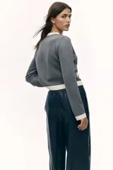 Cárdigan corto gris de punto fino con cuello redondo, cierre frontal con botones metálicos dorados y bolsillos decorativos con botón.