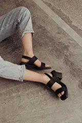 Sandalia de cuero color negro con taco bloque medio y punta cuadrada. Presenta dos tiras anchas sobre el empeine, una de ellas con hebilla metálica dorada, y una tira de sujeción en el talón. Posee base acolchonada para mayor comodidad.