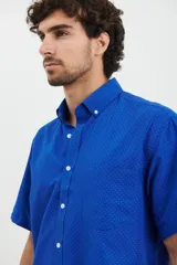 Camisa de manga corta azul con pequeños lunares blancos, cuello button-down y bolsillo en el pecho.