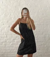 Vestido corto negro con estampado de líneas onduladas plateadas y tirantes de cadena metálica.